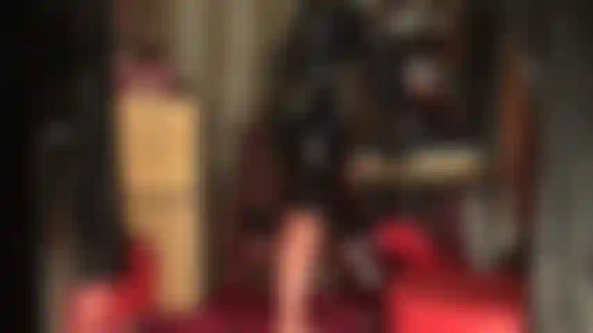 Un traje de goma brillante, medias y máscara. La diosa exhibe sus curvas con látex ajustado, medias transparentes con costuras, falda tubo negra y guantes. El traje se completa con una máscara de látex.