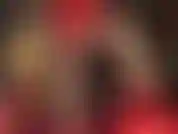 La ama se burla con sus muslos bien formados y sus piernas largas y delgadas en medias brillantes y pantalones cortos de satén rojo brillante.