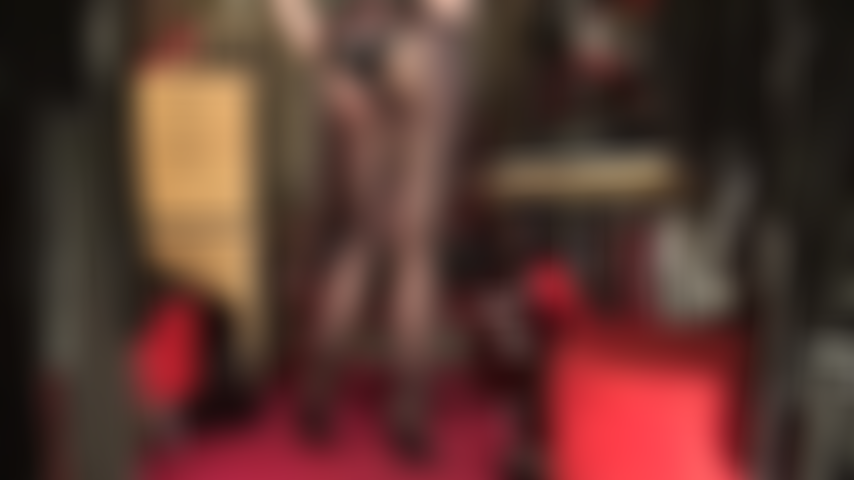 Piernas para morirse, vestida con medias de seda negras transparentes, pies en un par de sexis mules de cuero con tacones altos y un body de látex brillante para completar el look irresistible.