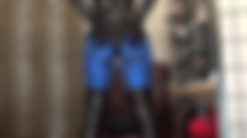 Culo en leggings de lycra azul metalizado y body de pvc brillante, pies en pantimedias marrón oscuro.