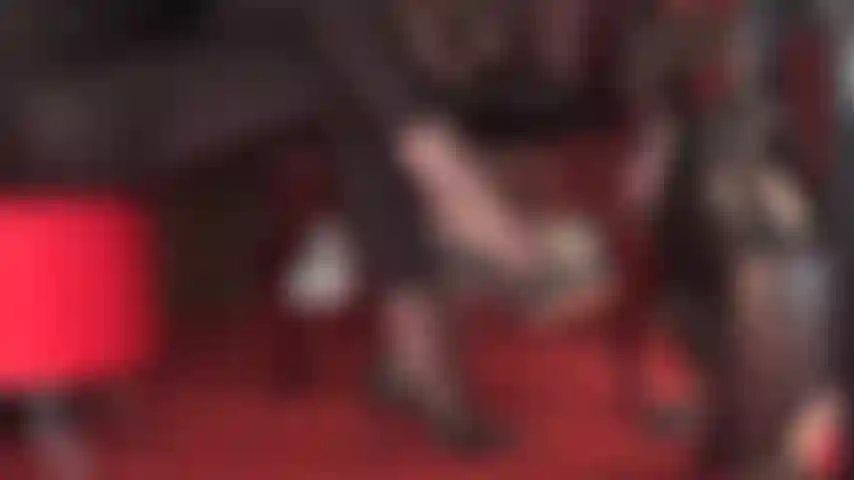 Disfruta de esta vista lateral de zapatos de tacón de cuero negro colgando en pantimedias y leggings de spandex brillante.