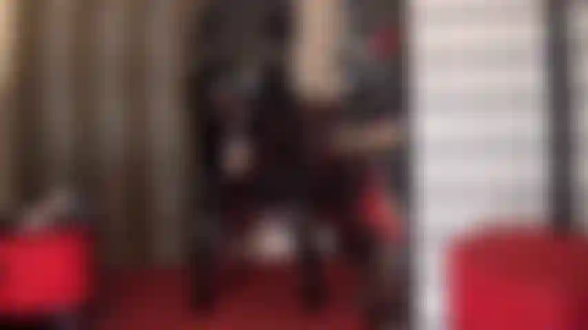 Una diosa de pvc en un brillante traje de gato negro que provoca con su enorme polla blanca con correa que se asoma por debajo de la capa de su falda.