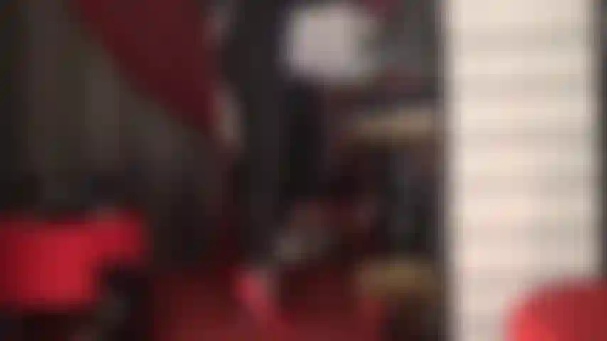 Tacones fetichistas de aguja rojos y tanga de encaje rojo sobre traje de gato negro ajustado.