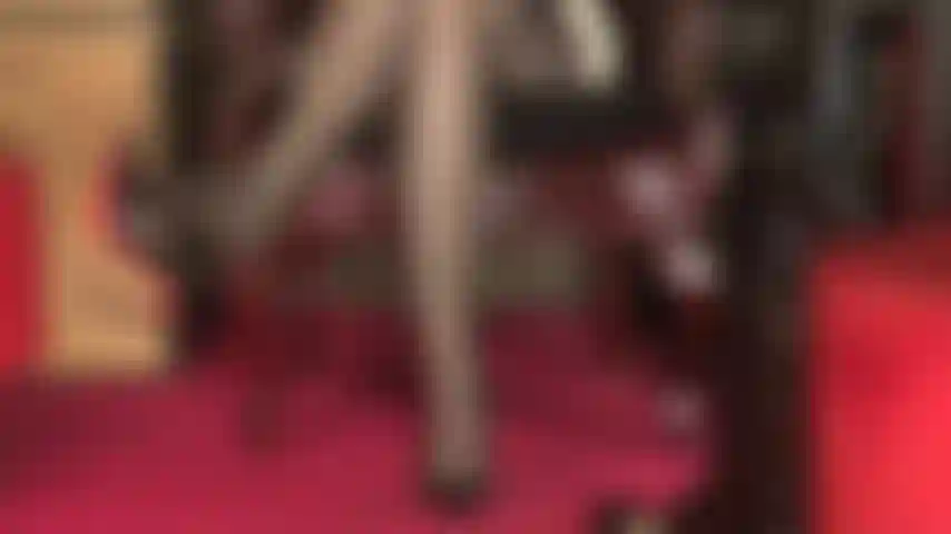 Una vista sexy de piernas cubiertas con medias, liguero con múltiples tiras que se asoma, muslos cruzados sexys y dedos de los pies que dejan colgando un zapato de suela roja.