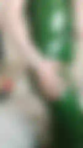 Cliente de latex, chat con un vestido de látex verde ceñido, de pie y sentada, mostrando las cremalleras del vestido, sin desnudez.